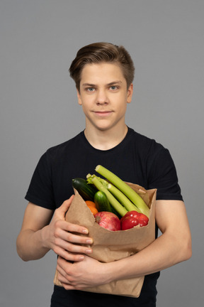 Joven mirando a la cámara con un bolsillo de papel lleno de frutas