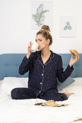 Vista frontale di una giovane donna in pigiama che fa colazione a letto