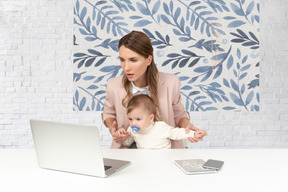 A woman holding a baby in front of a laptop