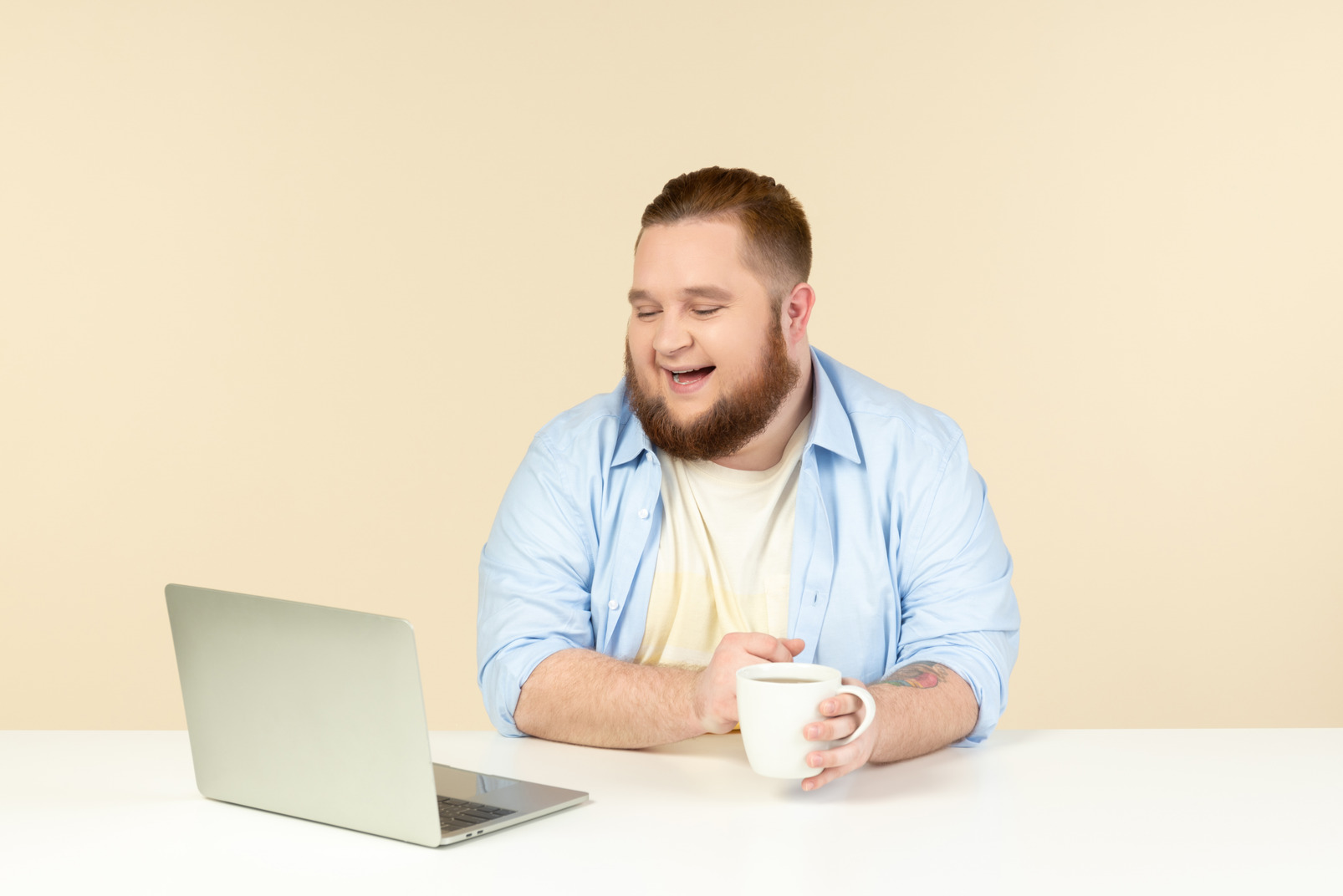 Laughing young overweight man looking at laptop and having tea