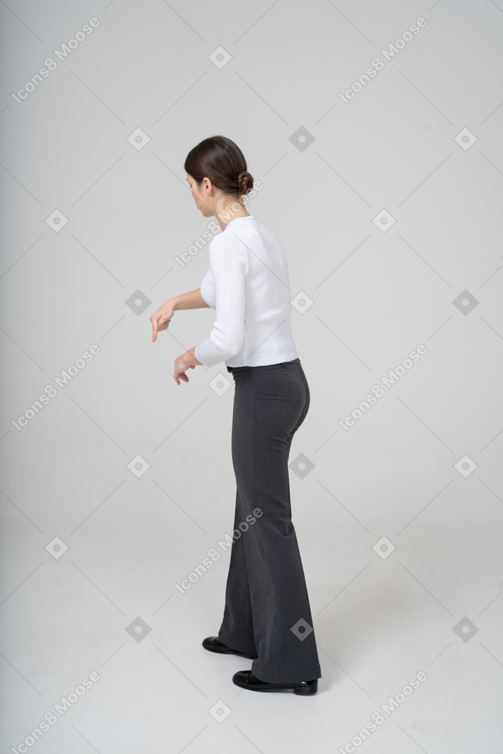 Вид сбоку молодой женщины в черных брюках и белой блузке, указывающей пальцем