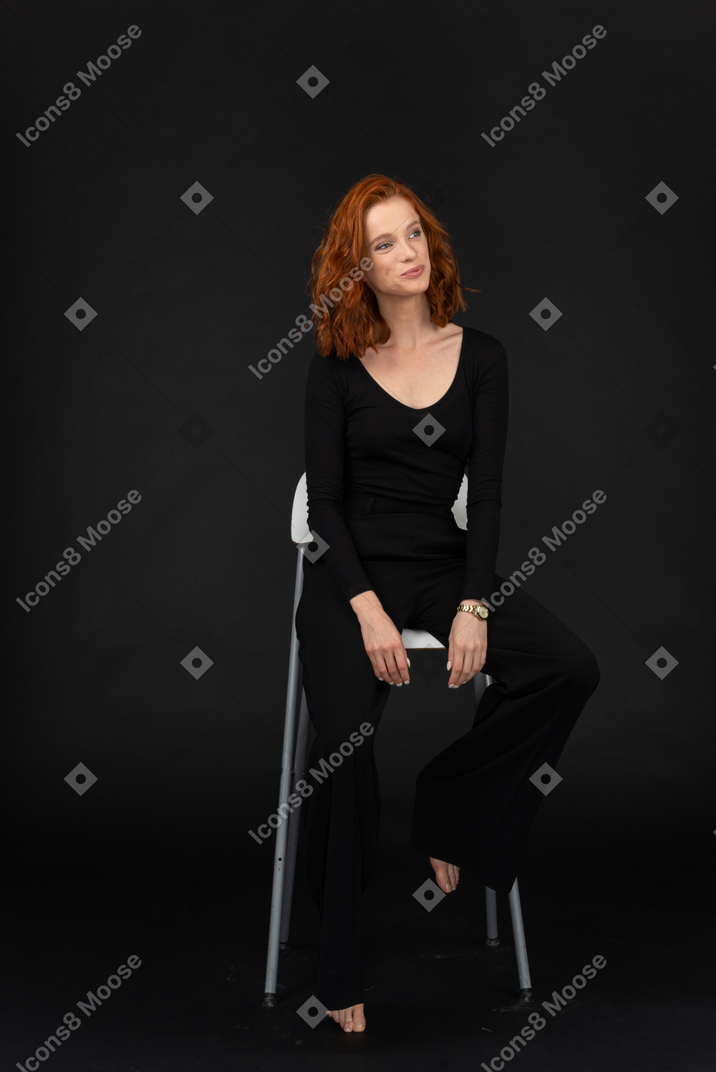 A frontal view of the beautiful woman dressed in black and sitting on the tall grey chair
