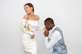 Groom kissing his bride's hand and she's holding a bouquet and smiling