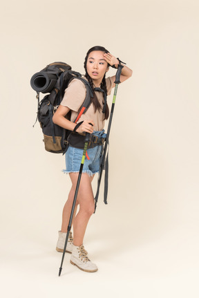 Tired hiker woman walking using trekking poles and drying her forehead with hand