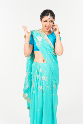 Wütend aussehende junge indische frau im blauen sari am telefon sprechen