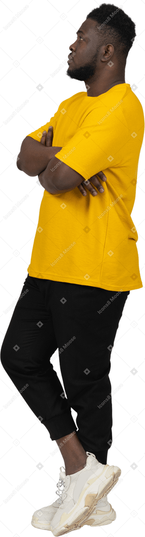 Dreiviertelansicht eines verdächtigen jungen dunkelhäutigen mannes in gelbem t-shirt, der die arme verschränkt