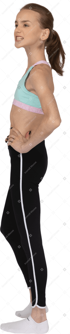 Vue latérale d'une adolescente en tenue de sport grimaçant et mettant les mains sur les hanches