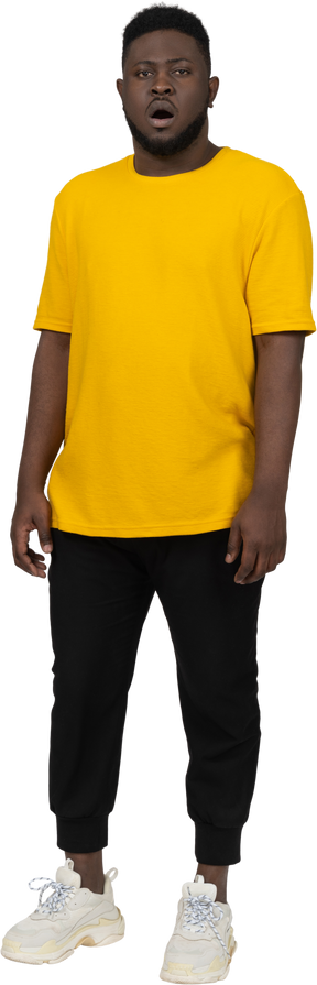 Vista frontal de un asombrado joven de piel oscura con camiseta amarilla parado
