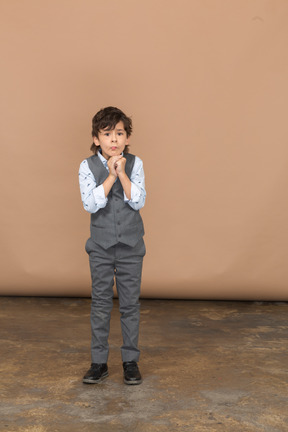 Вид спереди милого мальчика в сером костюме, делающего молитвенный жест