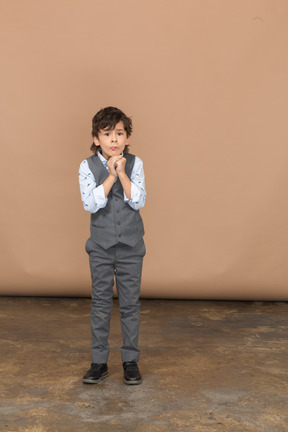 Vista frontal de un chico lindo con traje gris haciendo un gesto de oración