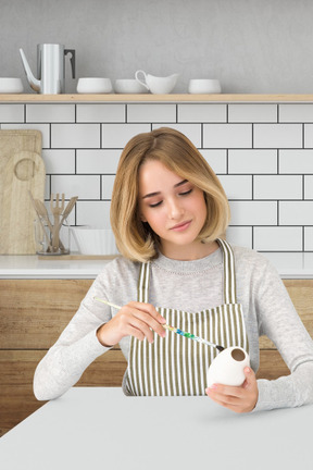 A woman in an apron applying paint on a ceramic object