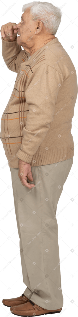 Side view of an old man in casual clothes touching nose