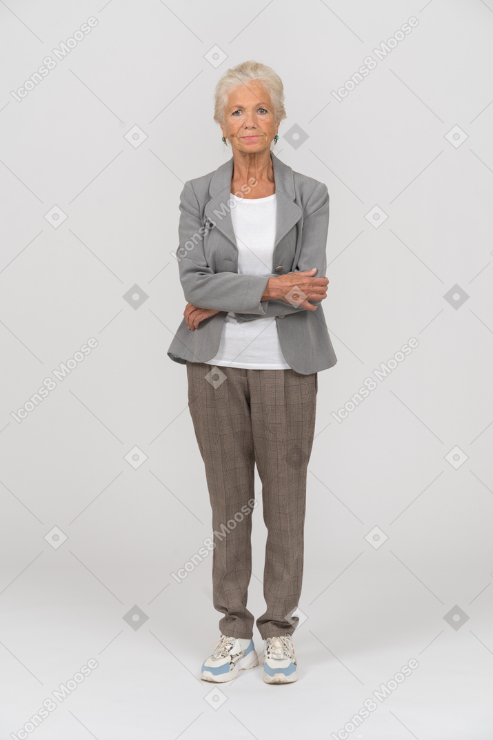 Front view of an old lady in suit standing with crossed arms and looking at camera
