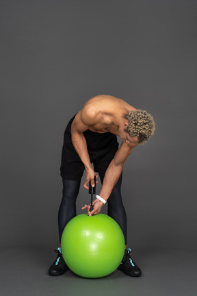 Vista frontale di un uomo afro a torso nudo che gonfia una palla da ginnastica