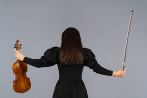 Vue arrière d'une joueuse de violon en robe noire écartant les mains