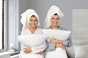 Two women in robes holding pillows and smiling