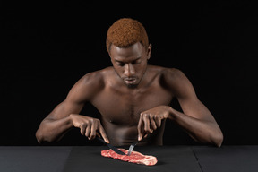 Front view of a young afro man cutting meat