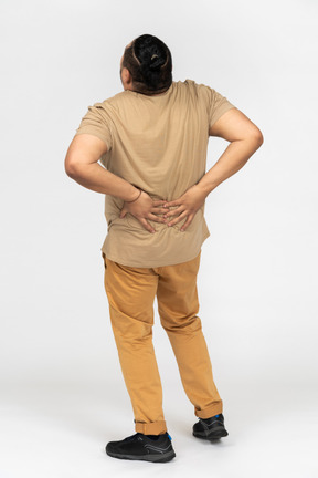 Азиатский человек, страдающий от болей в спине и удерживающий его поясницу обеими руками