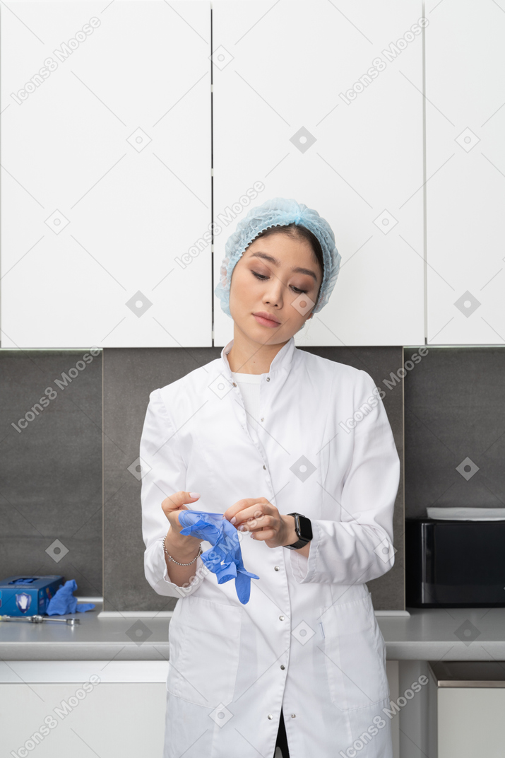 穿上防护手套在她的医疗柜里的年轻女医生的前视图