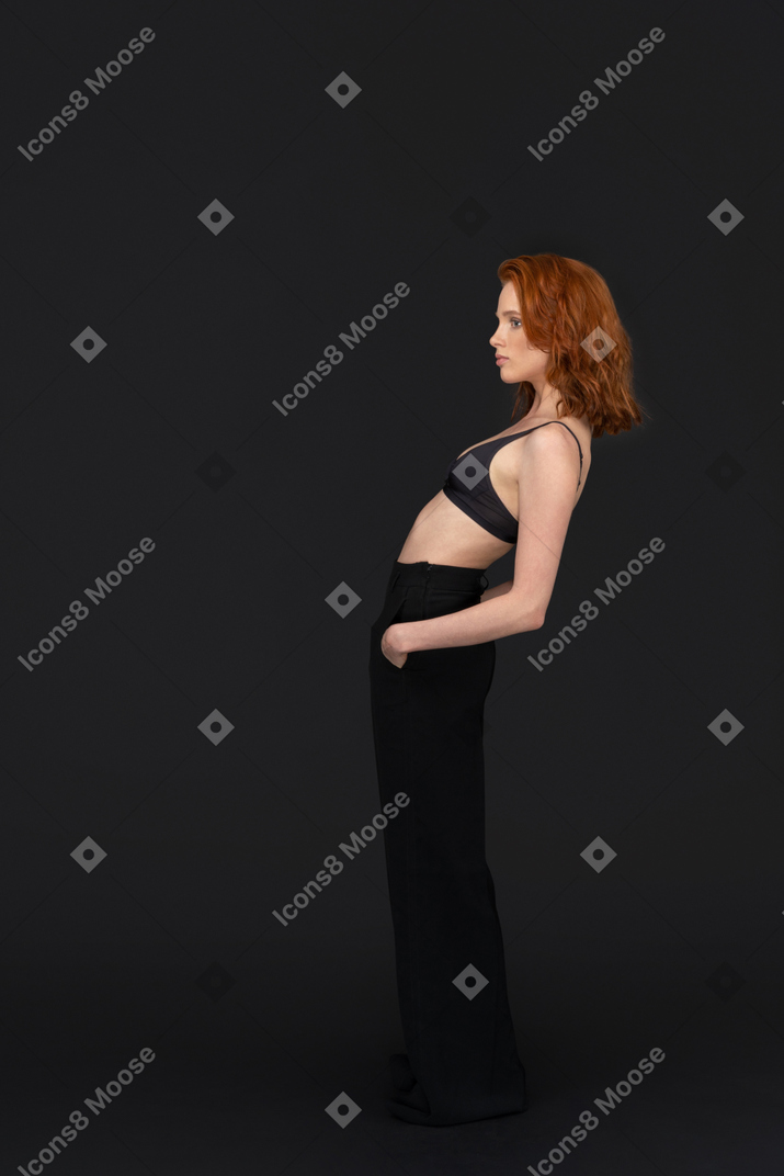 A side view of the sexy young woman standing on the black background looking to the left