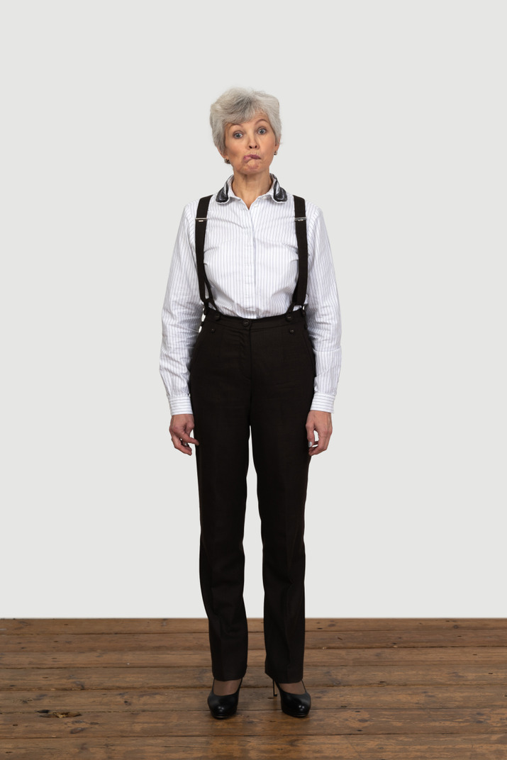 Front view of an old grimacing female in office clothes biting her lip with eyes wide open