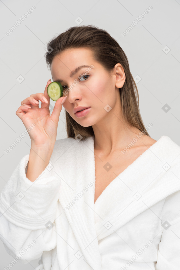 Belle jeune femme tenant une tranche de concombre