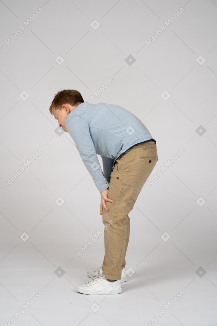 Side view of a cute boy bending down and touching knee