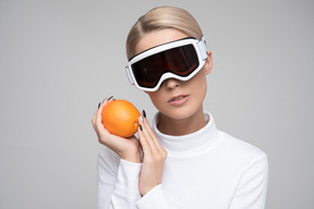 Joven rubia con gafas de esquí sosteniendo naranja
