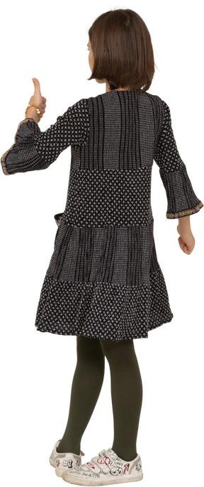 Three-quarter back view of a little girl in dress looking at camera and showing thumb up