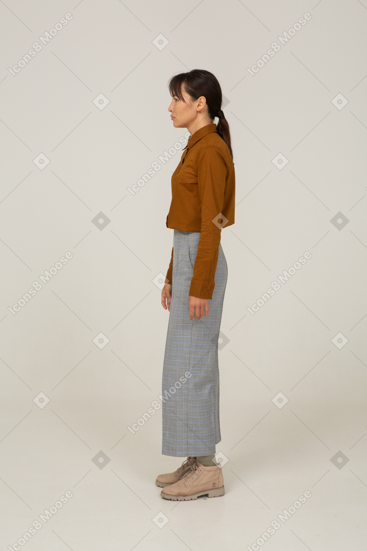 Vue latérale d'une jeune femme asiatique perplexe en culotte et chemisier debout immobile