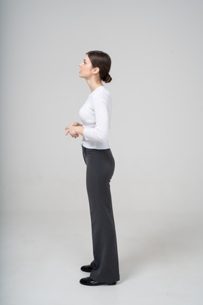 Молодая женщина в черных брюках и белой блузке стоит в профиль