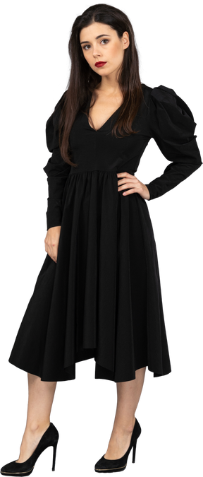 腰に手を置いている黒いドレスを着た若い女性の4分の3のビュー