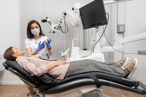 Toute la longueur d'une femme dentiste montrant un prototype de dents à une patiente dans une armoire d'hôpital