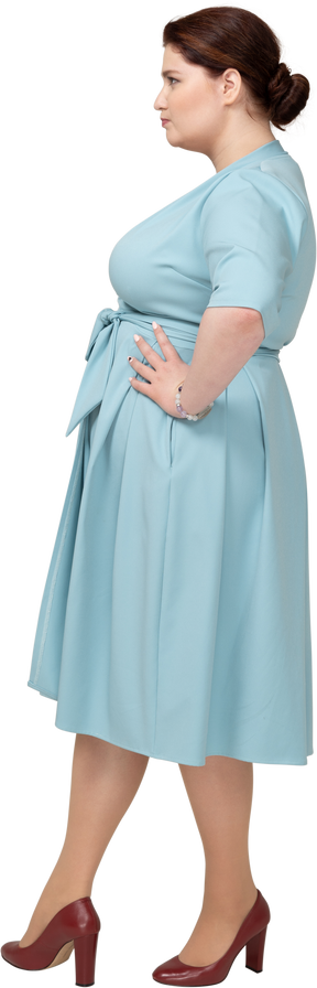 Вид сбоку женщины в синем платье позирует с руками на бедрах