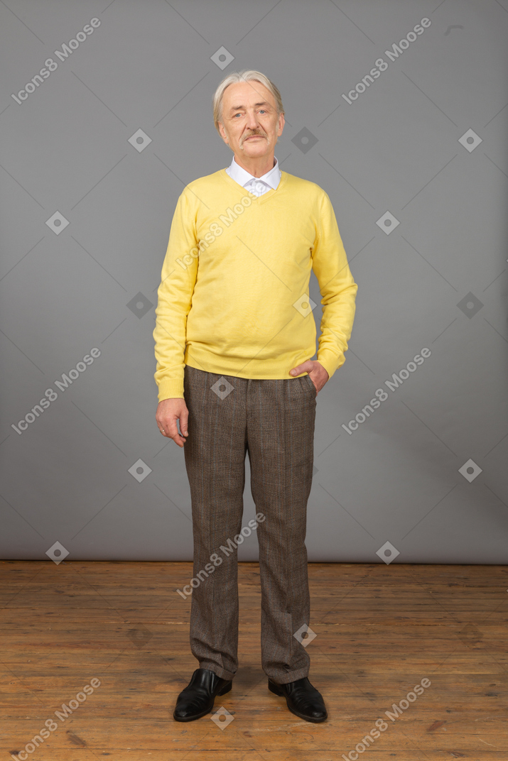 黄色のプルオーバーを着て、ポケットに手を入れて、カメラを見ている不機嫌な老人の正面図