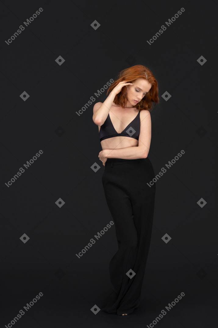 A frontal view of the sexy young woman standing on the black background looking down