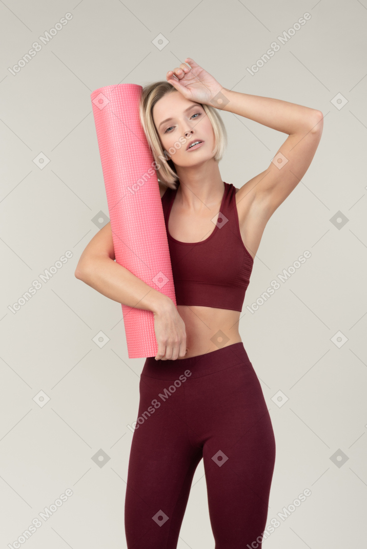 Mujer joven agotada en ropa deportiva con estera de yoga