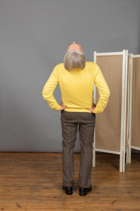 Back view of an old man putting hands on hips while leaning back