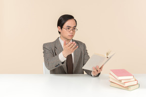 An asian teacher in a checkered suit, a tie and a book in his hand, working with the class