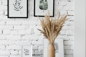 A vase filled with dry grass next to pictures on a wall