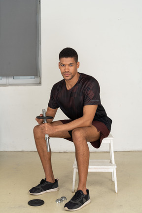 Young man in sports clothes sitting on white stool