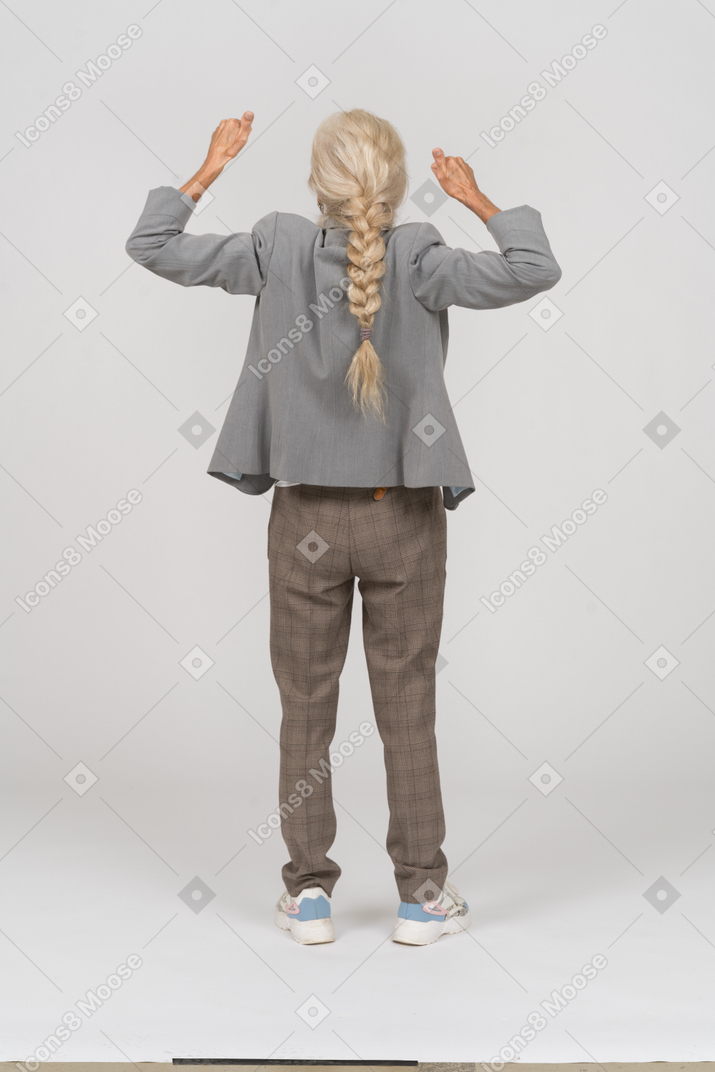 Rückansicht einer alten dame im anzug, die mit erhobenen händen steht