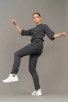 Side view of a young woman in a jumpsuit raising hands and leg