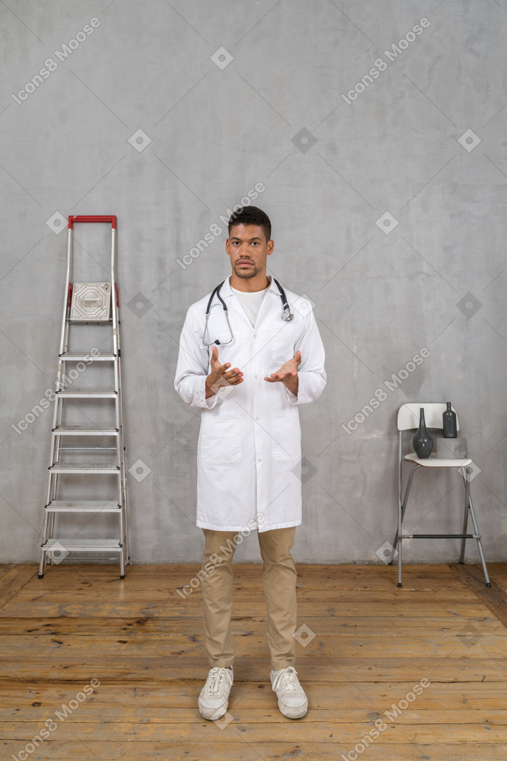 Vista frontale di un giovane dottore in piedi in una stanza con scala e sedia che spiega qualcosa