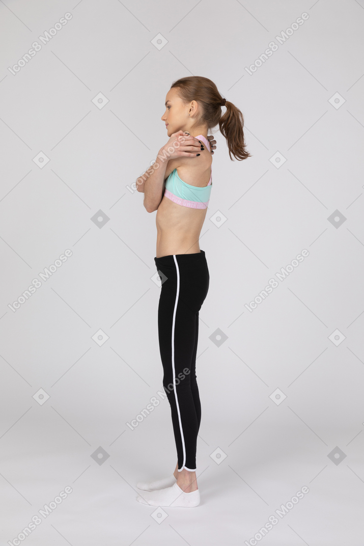 Side view of a teen girl in sportswear embracing herself