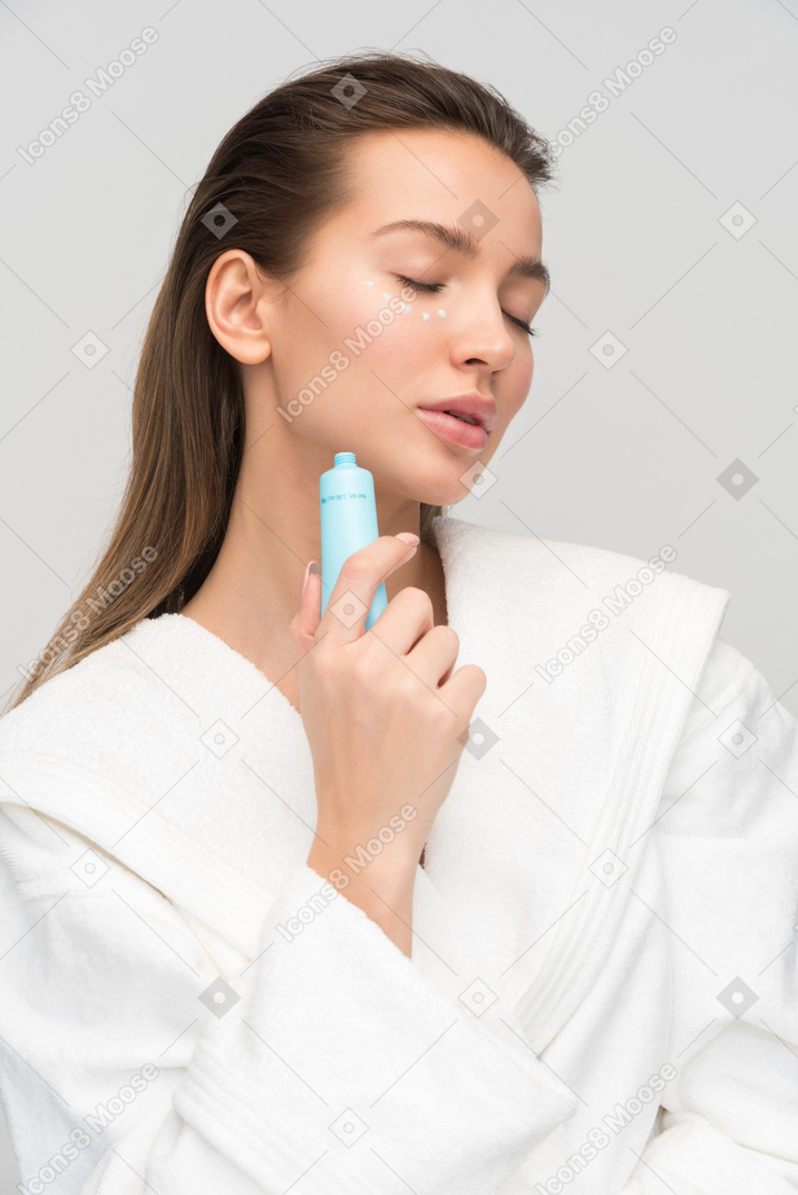 Beautiful young woman applying cream for eyes area