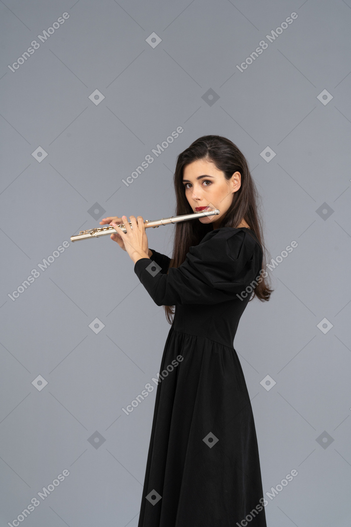 Side view of a serious young lady in black dress playing the flute