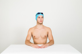 Bare chested swimmer sitting at the table with his hands on it