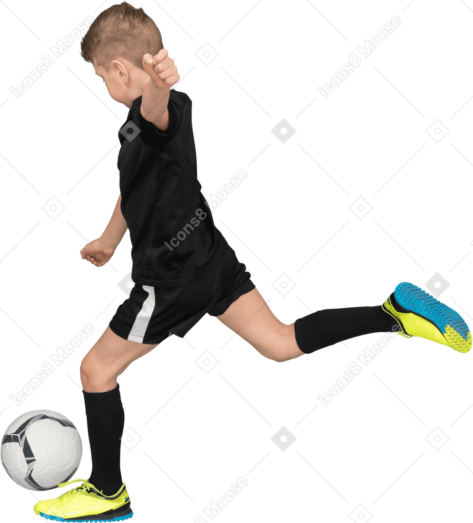 Vista lateral de um garoto com uniforme de futebol chutando uma bola