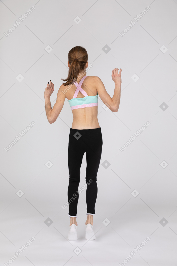 Back view of a teen girl in sportswear raising hands while jumping